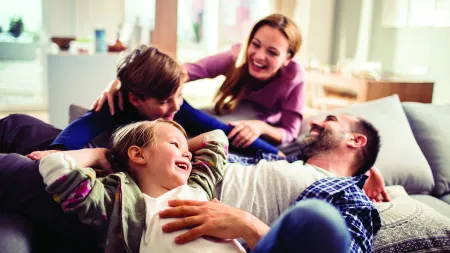 Happy family of four laughing and relaxing together on a cozy couch in a bright living room.