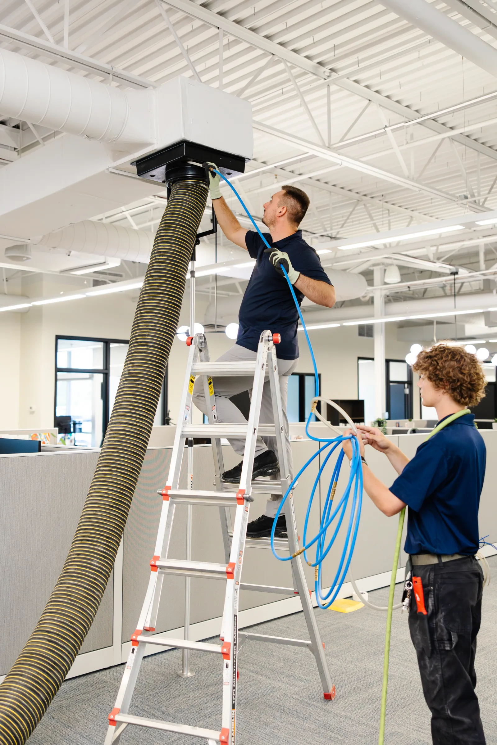 technician cleaning air ducts with assistant in office commercial building