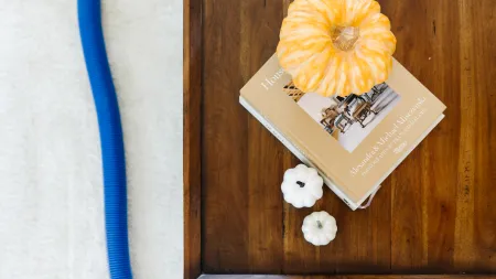 Colorful pumpkins atop a coffee table book, creating a cozy autumn-inspired decor setting with a zerorez carpet cleaning hose in the background.