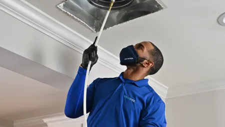 Technician cleaning HVAC duct with specialized equipment in a modern home environment.